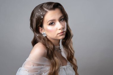 Kahverengi gözlü bir gelin portresi ve beyaz bir gelinlik içinde uzun kıvırcık saçlar ve inci desenli 