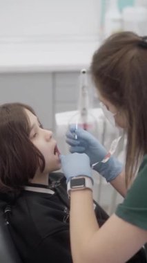 Bir pediatrik diş hekimi bir çocuğun dişlerine florür sürer. Caries 'i önlemek ve oral sağlığı korumak için düzenli florasyon. Hasta dişçinin ofisinde..