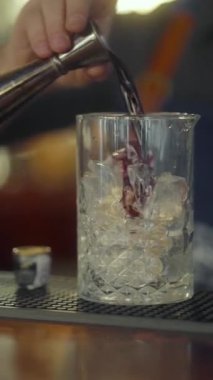 Bir barmen, bardaktaki jigger 'dan sert kırmızı bir alkolü ezilmiş buzla soğuk bir bardağa boşaltır. Restoran barında alkollü kokteyl yaparken dikey çekim..