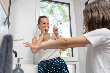 A mother and child playfully splash each other with water from their wet hands after their morning wash in the bathroom. The mom and her son have fun in the bathroom during their morning routine. clipart