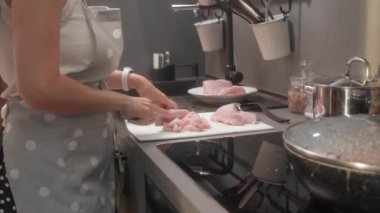 Önlüklü bir kadın keskin bir bıçakla çiğ hindi filetosunu küçük parçalara ayırıyor. Öğle yemeği için kümes hayvanları hazırlıyor..