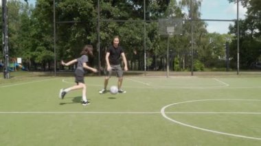 İki çocuk açık havada basketbol oynuyor. Ağabeyi, küçüklere top sürmede ve defansta rehberlik eder, yoldaşlıklarını gösterir, eğlenceli bir öğrenme ve dostça bir oyunda neşeyi paylaşır..