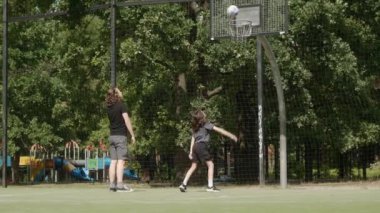 Basketbol sahasında iki adam basket atıyor, potaya girmeye çalışıyorlar. Top potayı ıskaladı, çembere ya da arka tahtaya çarptı. Iskalamalarına rağmen ateş etmeye devam ediyorlar..