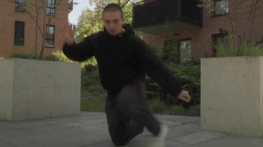 Dinamik bir sokak dansçısı, şehir ortamında, serbest stil hip-hop koreografisini sergileyerek enerjik hareketler sergiler. Sokak kültürü, kendini ifade etme ve halka açık bir yerde modern dans..