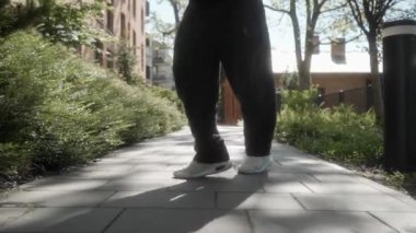 Neşeli bir adam güneşli bir kaldırımda yürüyor ve dans ediyor, sevinçten hoplayıp zıplıyor. Onun neşeli ayak hareketleri ve tasasız enerjisi şehir parkı ortamında mutluluk ve özgürlüğü yansıtıyor..
