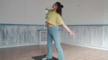 Genç bir kadın spor salonundaki bir paspasın üzerinde esneme egzersizleri yapıyor. Eğildi, büküldü, gerildi, esneklik ve kontrol gösterdi. Yoga, fitness ve egzersiz rutin gösterimi.