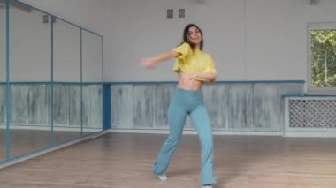 Genç bir bayan dansçı, akışkan dönüşler ve anlamlı hareketlerle dolu, dinamik ve çağdaş bir dans gösterisi gerçekleştiriyor. Stüdyonun açık alanı ve aynaları ideal bir prova ortamı yaratır..