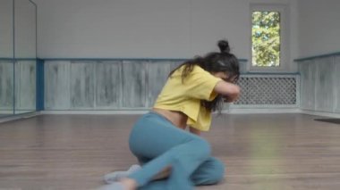 Dansçı dans eder, dans pistinde tüm vücudunu yuvarlar ve kaydırır. Kadın, modern dansın dinamik doğasını gösteren kolları ve bacaklarıyla zarif hareketler yapıyor..