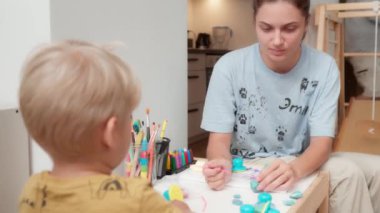 Annem çocuğuyla yaratıcı eğitim oyunları oynuyor. Anne ve oğlu çocuk masasında plastikten heykel yapıyorlar. Evde boş vakit ve aile zamanı. İnce motor becerilerin geliştirilmesi için sınıflar.