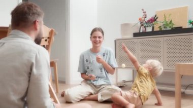 Genç ebeveynler odada yerde oturan küçük çocuklarıyla oynayıp dalga geçerek eğleniyorlar. Anne, baba ve oğul evde birlikte eğleniyorlar. Keyifli vakit ve aile zamanı..