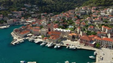 Deniz kenarındaki bir yamaçtaki turist kasabasının rıhtımı. Hırvatistan 'ın Brac (Sütyen) adasındaki Pucisca (Puia) liman kasabasında kiremit çatılı ve büyüleyici sokaklara sahip taş evler.