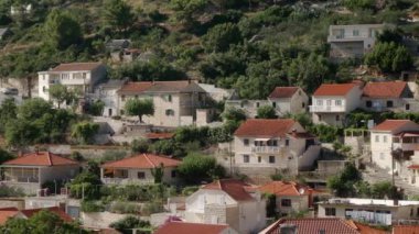 Tepenin yamacında, kiremitli çatıları olan eski taş evler. Hırvatistan 'ın Brac (Bra) adasındaki Pucisca (Puia) turizm kasabasının konut binaları ve sokakları. Akdeniz Mimari