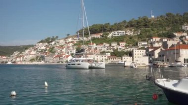 İçinde turist bulunan bir yelkenli katamaran, Hırvatistan 'ın Brac (Bra) adasındaki eski liman kenti Pucisca' nın (Puia) körfezine giriyor. Adriyatik kıyısı boyunca yat gezisi.