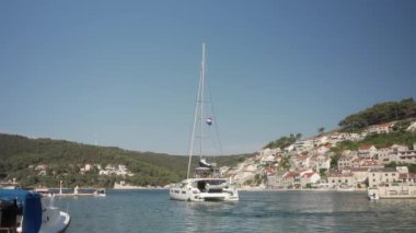 İçinde turist bulunan bir yelkenli katamaran, Hırvatistan 'ın Brac (Bra) adasındaki eski liman kenti Pucisca' nın (Puia) körfezinden ayrılıyor. Adriyatik kıyısında bir yat gezisi.
