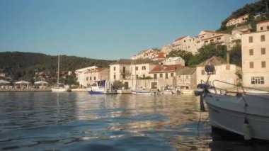 Deniz kıyısındaki eski bir kasabanın rıhtım güvertesi boyunca kıyıya demirlemiş tekneler. Hırvatistan 'ın Brac (Bra) adasındaki Pucisca (Puia) liman kasabasının konut binaları ve sokakları.