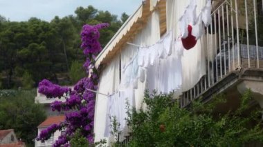 Çamaşır ipine asılmış ıslak çamaşırlar özel bir evin balkonunda kuruyor. Temiz beyaz iç çamaşırı, atlet ve mendiller rüzgarda sallanan mandallarla korunuyor. Çamaşır ve ev ödevi.