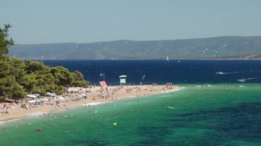 Hırvatistan 'ın Brac (Bra) adasındaki Zlatni Rat Sahili' nde güneşlenen, yüzen ve dinlenen turist kalabalığı görülüyor. Turizm sezonu boyunca Adriyatik Denizi kıyısında bir tatil. Dalgalar kıyıya çarpıyor..