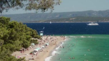 Hırvatistan 'ın Brac (Bra) adasındaki Zlatni Rat Sahili' nde güneşlenen, yüzen ve dinlenen turist kalabalığı görülüyor. Turizm sezonu boyunca Adriyatik Denizi kıyısında bir tatil. Dalgalar kıyıya çarpıyor..