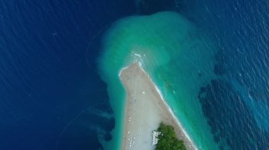 Hırvatistan 'ın Brac (Bra) adasındaki Zlatni Rat Sahili' nde insanlar güneşleniyor, yüzüyor ve dinleniyor. Adriyatik Denizi kıyısında bir turist tatili. Dalgalar geliyor ve kıyıda beyaz köpüğe dönüşüyor..