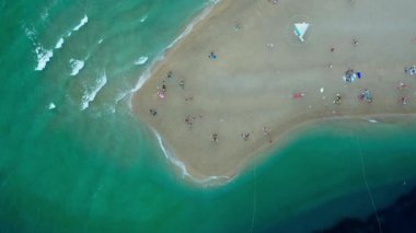 Hırvatistan 'ın Brac (Bra) adasındaki Zlatni Rat Sahili' nde insanlar güneşleniyor, yüzüyor ve dinleniyor. Adriyatik Denizi kıyısında bir turist tatili. Dalgalar geliyor ve kıyıda beyaz köpüğe dönüşüyor..