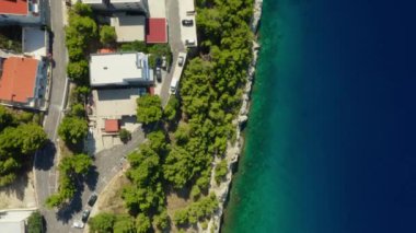 Sahilde yer alan oteller ve evler, çam ağaçlarıyla kaplı kayalık bir uçurum boyunca. Hırvatistan 'ın pitoresk Adriyatik kıyısında bir deniz kenti. Uçurumlar denizin derinliklerine doğru uzanıyor..