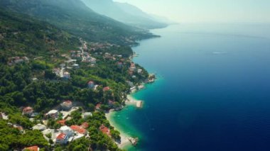 Adriyatik kıyısının pitoresk bir doğası. Hırvatistan kıyısındaki dağların eteklerindeki tatil beldeleri ve plajlar. Çam ağaçlarıyla kaplı kayalık sahil kıyısındaki turistik bir kasabada otel ve evler..
