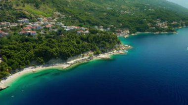 Adriyatik kıyısının pitoresk bir doğası. Hırvatistan kıyısındaki dağların eteklerindeki tatil beldeleri ve plajlar. Çam ağaçlarıyla kaplı kayalık sahil kıyısındaki turistik bir kasabada otel ve evler..