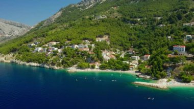 Adriyatik kıyısının pitoresk bir doğası. Hırvatistan kıyısındaki dağların eteklerindeki tatil beldeleri ve plajlar. Çam ağaçlarıyla kaplı kayalık sahil kıyısındaki turistik bir kasabada otel ve evler..