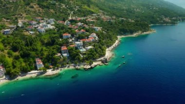 Sahildeki dağ yamacında oteller ve evler. Turistler plajda güneşlenir, denizde yüzer ve kürek çekerler. Hırvatistan 'ın pitoresk Adriyatik kıyısında bir sahil turizm kasabası.