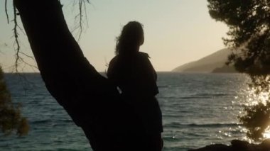 Bir kız gün batımını seyrediyor batan güneşin ışınlarında, sahildeki bir çam ağacının yanında duruyor. Deniz meltemi romantik bir şekilde saçlarını dalgalandırıyor. Hırvatistan 'daki Adriyatik kıyı dağlarının siluetleri.