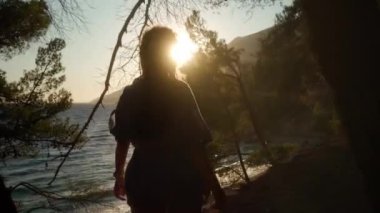 Kız, gün batımını ve Hırvatistan kıyılarındaki dağların siluetlerini seyrederek, batan güneşin ışınlarıyla deniz kıyısı boyunca çam ağaçları arasında geziniyor. Esinti saçlarını okşuyor..