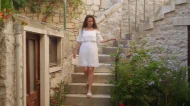 Beyaz elbiseli bir kadın, Akdeniz tarzında antik taş evleri olan büyüleyici bir caddeye doğru merdivenlerden iniyor. Bir kız Pucisca (Puia) kıyı kasabasında yürüyor).