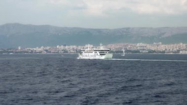 Split, Hırvatistan - 14 Temmuz 2024: Split-Supetar feribot hattına hizmet veren Jadrolinija şirketinin feribot feribotu, arka planda Split kentinin panoramik manzarasıyla kıyıya doğru yelken açıyor.