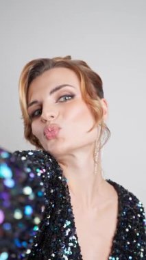 Kusursuz bir akşam makyajı, zarif bir updo ve pullu bir elbise ile güzel bir genç kadın selfie için poz verir, dudaklarını bir öpücüğe büzer ve pırıltılı elmas küpelerini gösterir..