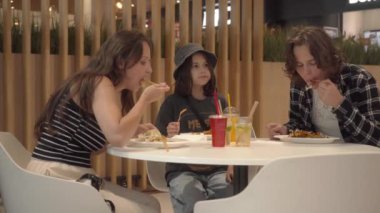 Çocuklarıyla birlikte bir kadın alışveriş merkezinin yemek katında yemek yiyor. Anne ve iki oğlu tek kullanımlık tabaklardan yiyip içerken aynı zamanda fast-food restoranlarının masasında oturuyorlar..