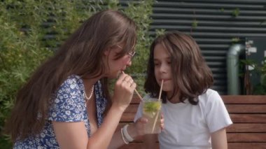 Bir kadın ve bir çocuk, parkta bir bankta otururken aynı bardaktan çıkan kamışla buz gibi limonata içiyorlar. Anne ve oğul sıcak bir yaz gününde ferahlatıcı bir içki paylaşırlar..