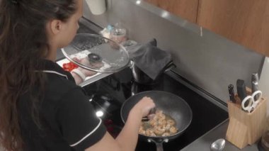 Evde karides pişirme süreci. Bir kadın bir elinde cam kapağı tutuyor ve spatulayla karidesleri karıştırıyor, onları sıcak, yapışmaz bir tavada kızartıyor..
