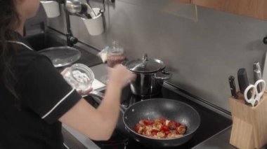 Bir kız yemeği tuzlar ve malzemeleri plastik bir spatulayla karıştırır. Kadın karides ve vişneli domates pişiriyor, evdeki elektrikli ocakta tavada kızartıyor.