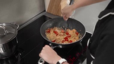 Bir kadın karides ve vişneli domatesli makarna pişiriyor. Kız yemeğin malzemelerini çubuksuz bir tavada spatulayla karıştırıyor. Bir ev hanımı deniz ürünleri yemeği hazırlar..