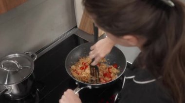 Bir kadın karides ve vişneli domatesli makarna pişiriyor. Kız yemeğin malzemelerini çubuksuz bir tavada spatulayla karıştırıyor. Bir ev hanımı deniz ürünleri yemeği hazırlar..