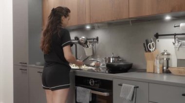 Bir kız cam kapağı çıkarıyor ve kızartma tavasına doğranmış kabak ekliyor. Malzemeleri spatulayla karıştırıyor. Kadın, kahvaltıda sebze tabakları pişiriyor..