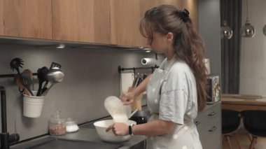 Bir kadın ölçü kabını kullanarak sıvı hamura un döker ve çırpıcıyla karıştırır. Ev mutfağında yemek hazırlıyor, içindekileri bir kasede birleştiriyor. Ev yapımı tarifle krep yapmak..