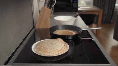 Tabakta bir yığın kavrulmuş gözleme. Onun yanında, krep kızartma tavasında kızarır. Adam bitmiş gözlemeyi bir spatulayla çevirir ve tavadan çıkarır..