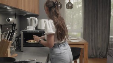 Bir kadın mikrodalgayı açar, ısıtılmış bir tabak krep alır ve masaya koyar..