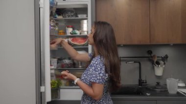 Bir kadın evdeki mutfaktaki buzdolabından omlet yapmak için malzeme alıyor. Buzdolabını açar, yumurtaları ve bir şişe inek sütü çıkarır ve kapıyı kapatır..