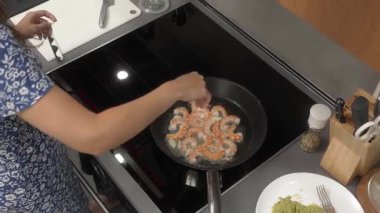 Bir kadın, sarımsak ve tereyağlı tavada kızartılan bir tutam tuzlu karidesi tuzluyor. Evde indüksiyon sobasında vejetaryen deniz ürünleri tabağı hazırlıyor..