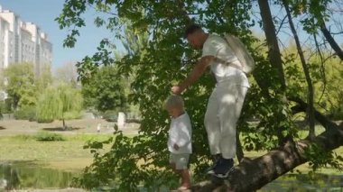 Bir baba ve küçük oğlu, el ele tutuşmuş, bir ağacın gövdesinde suyun üzerinde yürürken dengede duruyorlar. Baba çocuğuna zorluklara göğüs germeyi ve zorlukların üstesinden gelmeyi öğretir..