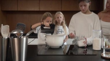 Anne ve kızlar mutfaklarında yemek pişirirler. Kız el karıştırıcı kullanıyor, kız kardeş şeker ekliyor. Annem bu neşeli aile yemeklerine, takım çalışmalarına ve aşçılık becerilerine rehberlik eder..