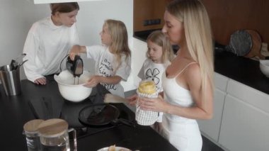En büyük kız, aile mutfağında krep hamuru ile el karıştırıcısını karıştırıyor. Annem ve küçük kız kardeşlerim, o yemek pişirmek için pürüzsüz hamur işini bitirirken dikkatle izleyin..