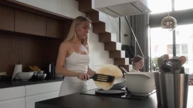 Becerikli anne kahvaltı hazırlarken tavada krep çeviriyor. Ev yapımı yemeği mükemmel pişirirken buhar yükseliyor ve kızı yemek pişirme etkinliğini izliyor..